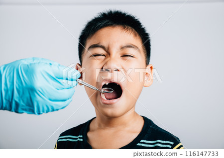 After removal of a child's loose milk tooth a pediatric dentist examines mouth using dental tools. Observation taking place in a dental office. Doctor uses mouth mirror to checking teeth cavity 116147733
