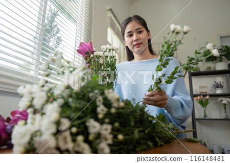 Woman Arranging Fresh Flowers at Home in a Bright and Modern Living Space with Natural Light 116148481
