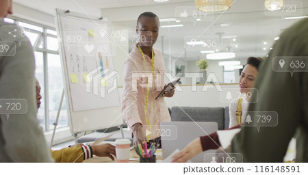 Anmation of social media icons over diverse team of fashion designers discussing together at office Anmation of social media icons over diverse team of fashion designers discussing together at office 116148591