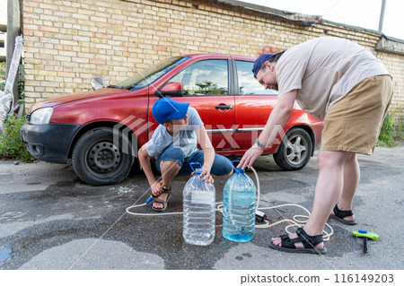 Dad and teenage son work together on the street near the garage. Outdoor activity. Family spend time. Helping and teach. Repairing a hose and pump for hand washing a car from a plastic bottle 116149203