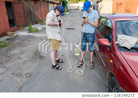 Dad and teenage son work together on the street near the garage. Outdoor activity. Family spend time. Helping and teach. Repairing a hose and pump for hand washing a car from a plastic bottle Dad and teenage son work together on the street near the garage. Outdoor activity. Family spend time. Helping and teach. Repairing a hose and pump for hand washing a car from a plastic bottle 116149233