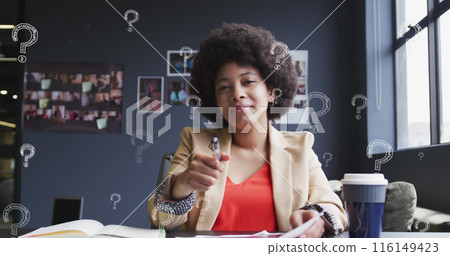 Image of question mark symbol over biracial businesswoman with afro hair writing in book 116149423