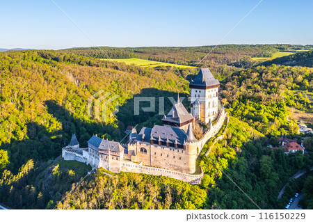 Aerial perspective of Karlstejn Castle nestled in a forested landscape with surrounding lush greenery on a clear, sunny day in Czechia. Aerial view from drone. 116150229