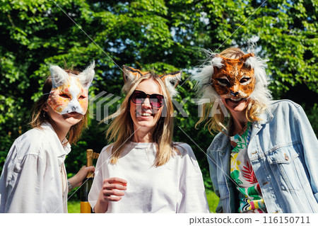 Three young adult beautiful woman girls friends enjoy have fun wearing animal mask laughing at picnic party city park green garden at sunny day. Female person friendship summer outdoors celebration Three young adult beautiful woman girls friends enjoy have fun wearing animal mask laughing at picnic party city park green garden at sunny day. Female person friendship summer outdoors celebration 116150711