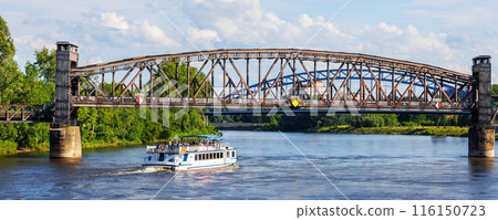 Tourist boat cruises under old historic iron bridge on Elbe River in Magdeburg, Germany with blue sky clouds background landscape. Saxony-Anhalt center cityscape sightseeing water trip 116150723