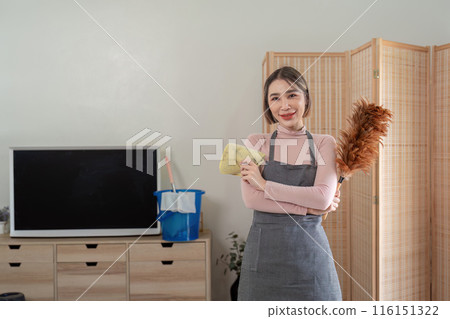 Housekeeper Smiling While Holding Cleaning Tools in a Modern Living Room Setting 116151322