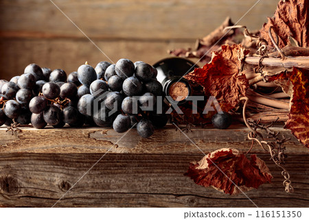Bottle of red wine with grapes and dried vine on an old wooden table. Bottle of red wine with grapes and dried vine on an old wooden table. 116151350