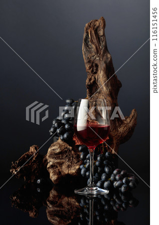 Glass of red wine with an old snag and blue grapes. 116151456
