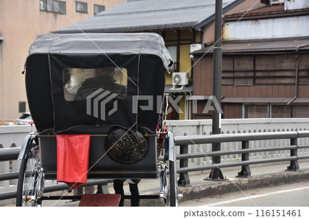 Takayama City, Gifu Prefecture, Japan: A rickshaw crossing a bridge in the center of the city. The old townscape and the back of the vehicle carrying tourists. 116151461