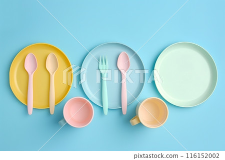 Baby feeding accessories, tableware, cutlery set on blue background. First dishware for kids concept. Flat lay, Top View, Copy space. Silicone dishware, cup. Solid color backdrop. Serving baby food 116152002