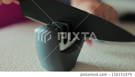 Closeup woman hands sharpens knife with special knife sharpener. Knife sharpening. Closeup woman hands sharpens knife with special knife sharpener. Knife sharpening. 116152879