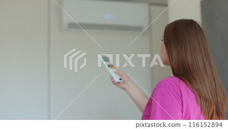 Woman feels hot and turning on remote control air conditioner at home. Stream of cold air from a split system. 116152894