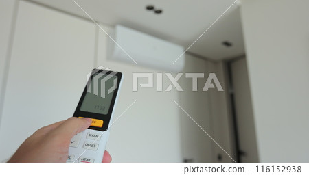 Process of turning on the air conditioner in the home living room. Man selects temperature of air cooling in home with of modern technologies. Hand uses air conditioner remote control. 116152938