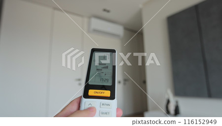 Man adjust the temperature on air conditioner in the living room. Hand uses air conditioner remote control. 116152949