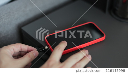 Man hands plugging a charger in a smartphone on bedside table. Mobile smartphones charging. Man hands plugging a charger in a smartphone on bedside table. Mobile smartphones charging. 116152996