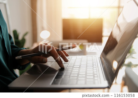 Female Manager Using Laptop Computer To Check Inventory. In the Background Warehouse Retail Center with Cardboard boxes, e-Commerce Online Orders, Food, Medicine, Products Supply. Over the Shoulder Female Manager Using Laptop Computer To Check Inventory. In the Background Warehouse Retail Center with Cardboard boxes, e-Commerce Online Orders, Food, Medicine, Products Supply. Over the Shoulder 116153058