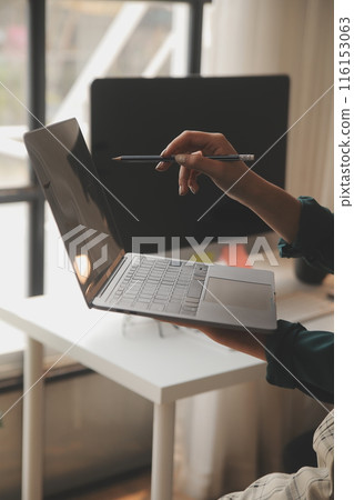 Female Manager Using Laptop Computer To Check Inventory. In the Background Warehouse Retail Center with Cardboard boxes, e-Commerce Online Orders, Food, Medicine, Products Supply. Over the Shoulder 116153063