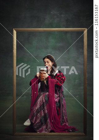 Portrait of beautiful medieval queen royal person in luxurious period attire sipping lager foamy beer against vintage green background. Oktoberfest traditions 116153167