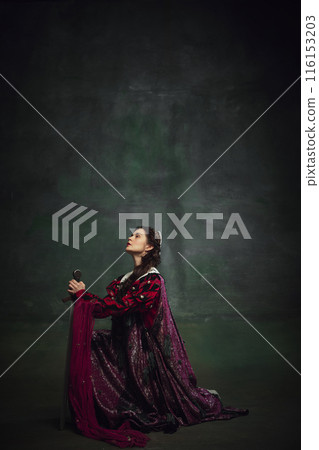 Young elegant woman sitting in dramatic pose with sword against vintage green background. Film industry, strong female characters 116153203