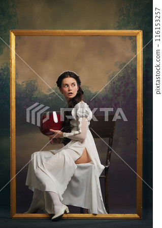 Escaping from reality with alcohol drink. Portrait of beautiful young woman, medieval royal person in white dress sitting on picture frame with wine glass Escaping from reality with alcohol drink. Portrait of beautiful young woman, medieval royal person in white dress sitting on picture frame with wine glass 116153257
