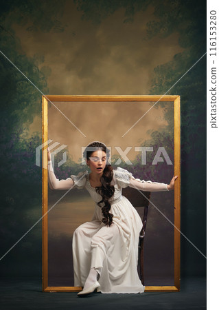 Emotional elegant young woman in white dress sitting inside golden picture frame and looking around. Looking into unknown Emotional elegant young woman in white dress sitting inside golden picture frame and looking around. Looking into unknown 116153280