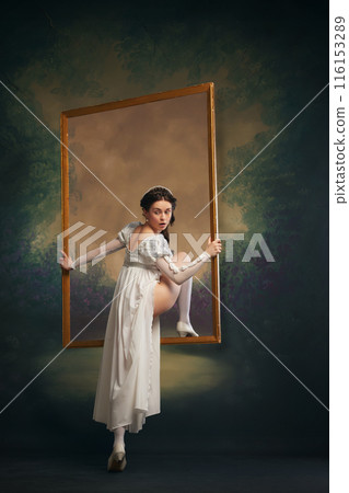 Romanticizing past. Beautiful and sensual young women in medieval white dress stepping into picture frame on vintage background. Aesthetic of Victorian era Romanticizing past. Beautiful and sensual young women in medieval white dress stepping into picture frame on vintage background. Aesthetic of Victorian era 116153289