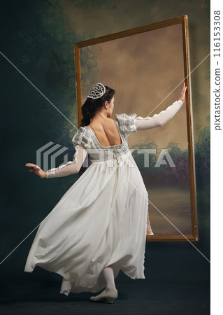 Vintage Escape. Elegant young woman in white dress stepping into picture frame against vintage background. Historical romance Vintage Escape. Elegant young woman in white dress stepping into picture frame against vintage background. Historical romance 116153308