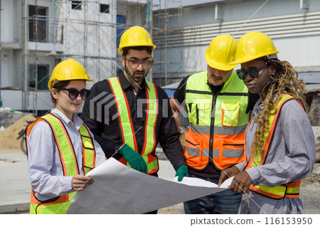 Group of construction worker gathered at a construction site reviewing some plan. Unfinished building, piles of construction material, and a partially constructed structure are in the background Group of construction worker gathered at a construction site reviewing some plan. Unfinished building, piles of construction material, and a partially constructed structure are in the background 116153950