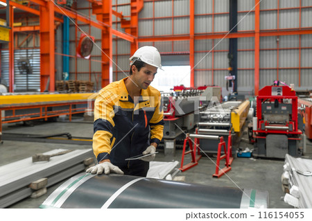 Industrial diligent worker safeguarded by a hard hat, engrossed in his duties amidst the complex machinery of a bustling factory. 116154055