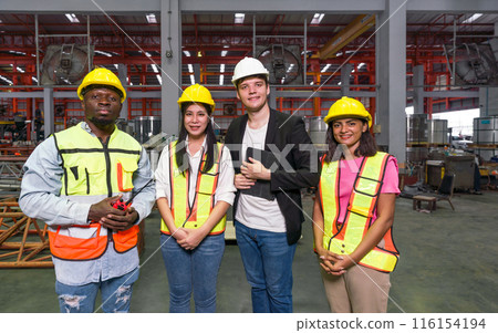 A smiling team of worker stand together for a group photo inside a factory with machinery in the background. A smiling team of worker stand together for a group photo inside a factory with machinery in the background. 116154194