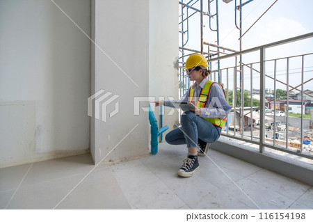 A construction worker is inspecting a building site. They are wearing safety gear and checking plumbing installation indoor. A construction worker is inspecting a building site. They are wearing safety gear and checking plumbing installation indoor. 116154198