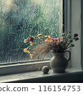 Image of a windowsill with flowers and a vase on the window, with rain falling outside 116154753