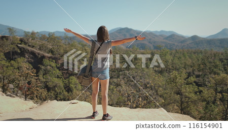 Tourist woman relaxes in Pai Canyon Kong Lan enjoying aerial mountain landscape. Caucasian girl rising hands looking at beautiful forest and mount range. Travel to Thailand, Chiang Mai Province. 116154901