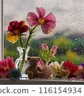 Image of flowers and vase on the window sill with teddy bear and rain outside 116154934
