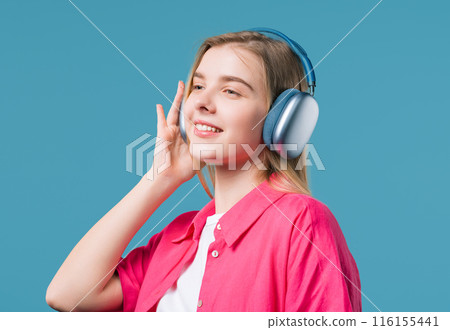Blonde 20s woman listening streaming music, dancing with headphones on blue Blonde 20s woman listening streaming music, dancing with headphones on blue 116155441