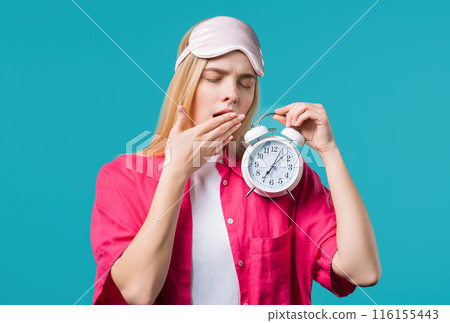 Woken up by alarm clock sleepy young woman holding it in hand. Blue background 116155443