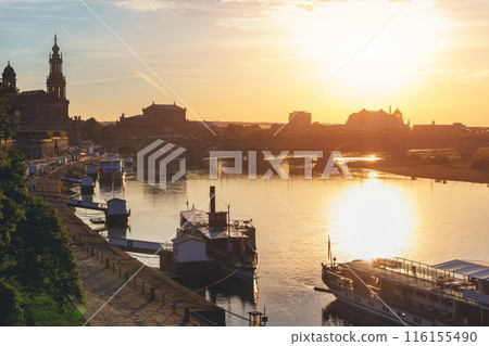 Scenic warm sunset beautiful Dresden city skyline at Elbe River with many steam tourist ship vessel moored at bank. Saxony Germany capital cityscape dusk panoramic view with old Europe architecture 116155490