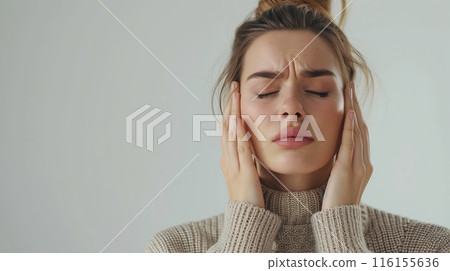 Woman covers ears with hands in discomfort, likely from a headache 116155636