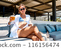 young girl in summer dress and swimwear resting at the sunny beach, sitting at a cafe with a 116156474