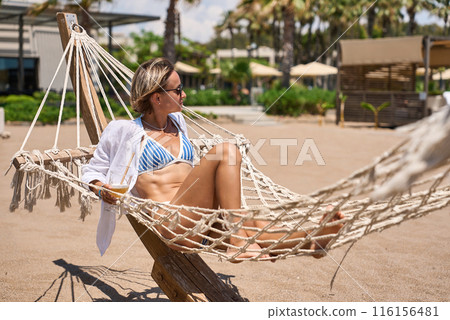 Enjoying summer vacation. Young happy woman relaxing while lying in the hammock on the sandy beach 116156481