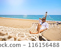 Enjoying summer vacation. Young happy woman relaxing while lying in the hammock on the sandy beach 116156488