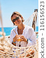 Enjoying summer vacation. Young happy woman relaxing while lying in the hammock on the sandy beach 116156523