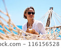 Enjoying summer vacation. Young happy woman relaxing while lying in the hammock on the sandy beach 116156528