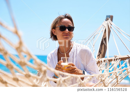 Enjoying summer vacation. Young happy woman relaxing while lying in the hammock on the sandy beach 116156528