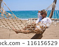Enjoying summer vacation. Young happy woman relaxing while lying in the hammock on the sandy beach 116156529