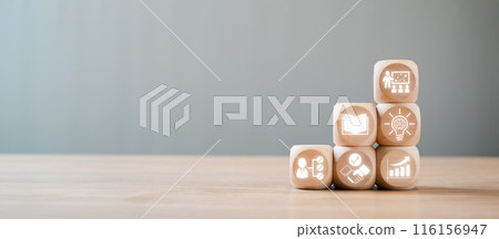 Wooden blocks with icons symbolizing capacity building, education, growth, and development on a wooden table against a neutral background. 116156947