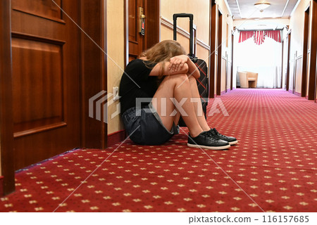 A woman sitting with a feeling of sadness and loss while traveling with a lot of luggage on the floor. The room is occupied. 116157685