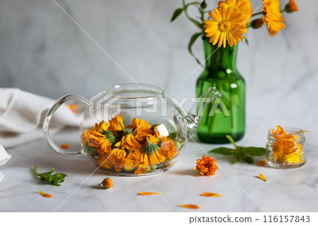 Cup of marigold tea and calendula flowers outdoors on green background. 116157843