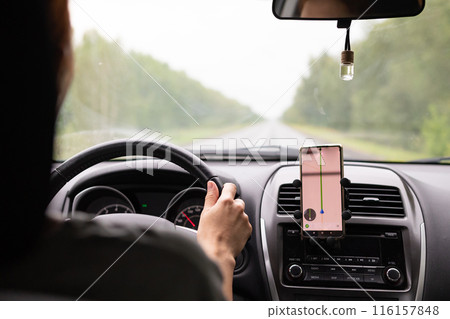 Rear view of a young traveler using a navigator on a mobile phone behind the wheel of a modern car . 116157848