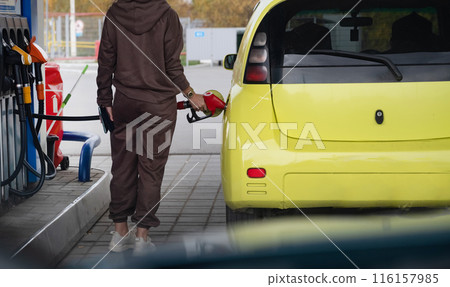 Attractive young woman refueling car at gas station. Female filling diesel at gasoline fuel in car using a fuel nozzle. Petrol concept. Side view 116157985